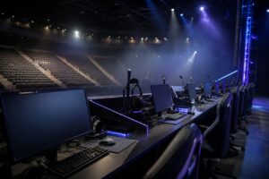 Tom e-sportscen med datorer och headset på borden i dämpat blått ljus och tomma publikplatser